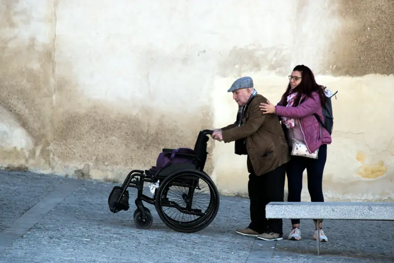 Žena podopiera staršieho muža, ktorý tlačí invalidný vozík